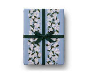 Gift box wrapped with white hydrangea floral light blue design gift wrapping; green velvet ribbon tied in finishing bow on top. Rifle Paper Co. 