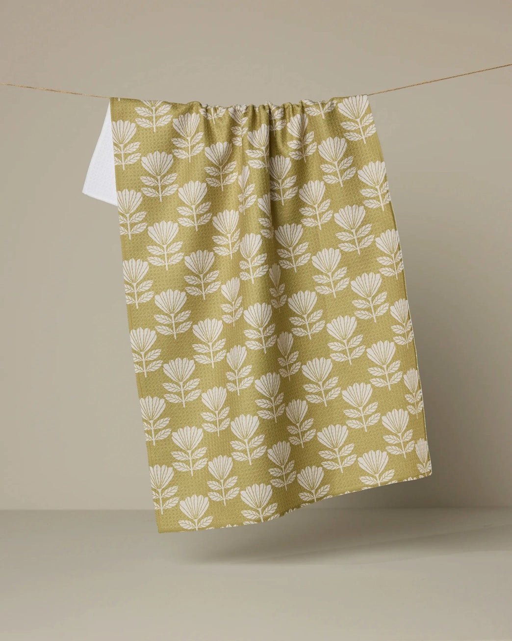 Yellow ochre kitchen and bathroom towel with white floral folk pattern hanging on a line against a beige background. Geometry House. 