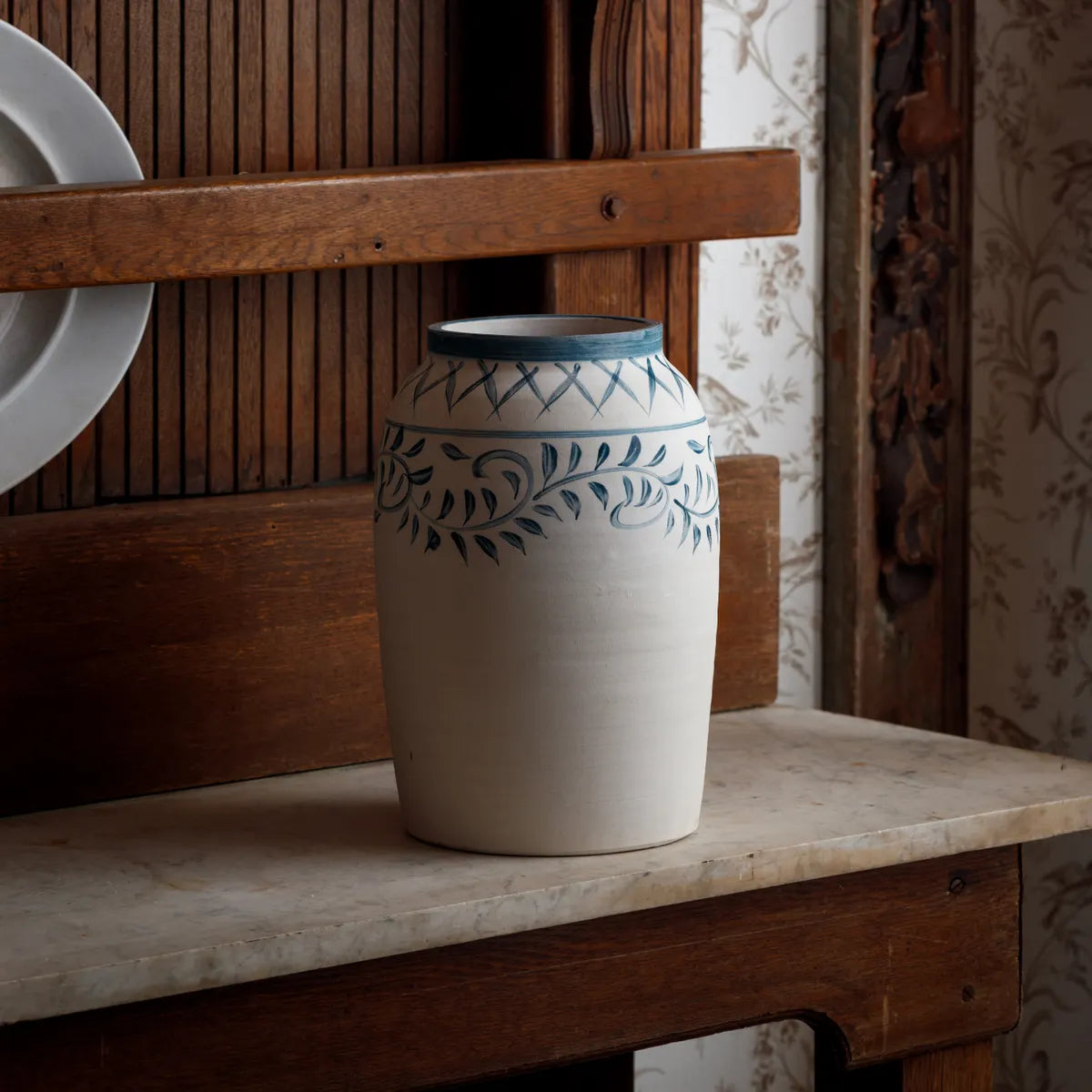 Ceramic olive jardin vase with hand painted blue floral motif patterns on a wooden shelf
