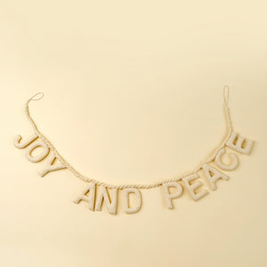Decorative ivory colored felt banner with 'JOY AND PEACE' text on a beige background.