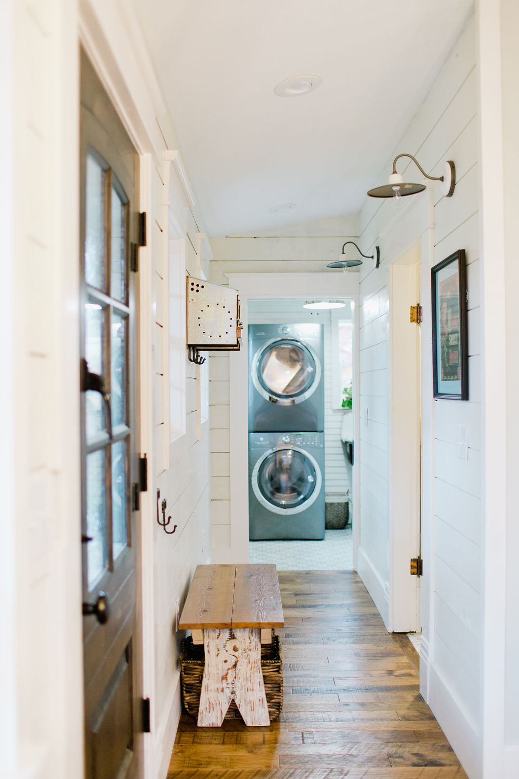 White hallway to a laundry room with country accents like rustic bench and shiplap