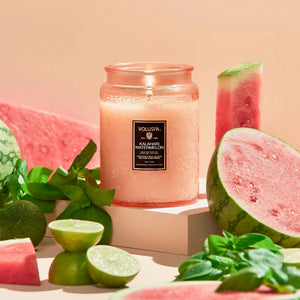 Voluspa Kalahari Watermelon candle nestled into a table display with watermelon and limes on a beige background.
