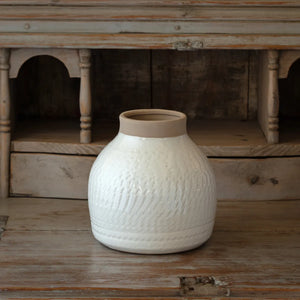 White textured terracotta vase on a wooden surface with a rustic wooden shelf in the background.