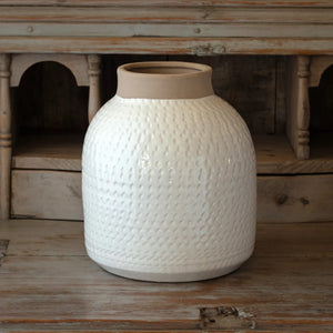 Larger version of a white textured terracotta vase on a wooden surface with a rustic background. 