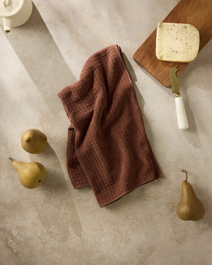 Maple brown waffle weave hand towel on a stone surface with pears and a cutting board. Geometry. 