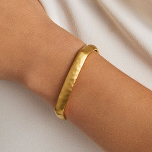 Gold bangle bracelet on a person's wrist against a neutral background