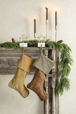 Holiday rustic wood mantel decorated with taper candles, garlands, and hanging stockings with a pair of gold and marble stocking angers. 