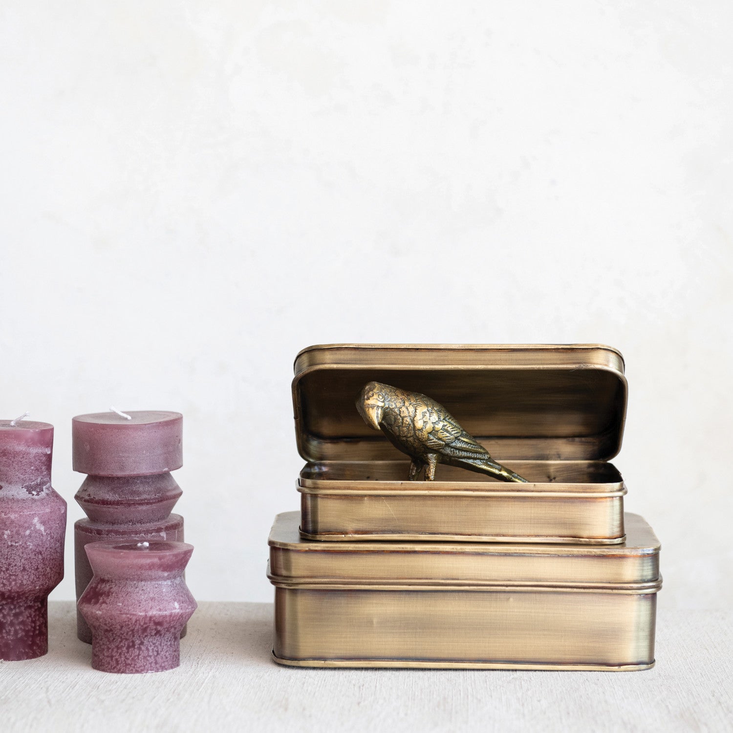 Antique brass decorative storage tins with a decorative bird figurine displayed inside on a white background