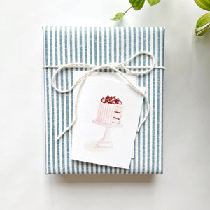 Blue and white tick striped wrapped gift with mini pink cake gift card attached to the front. Emily Lex studios. 