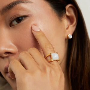 Close-up of a woman wearing a gold ring with a white Moonstone centerpiece, touching her cheek. 
