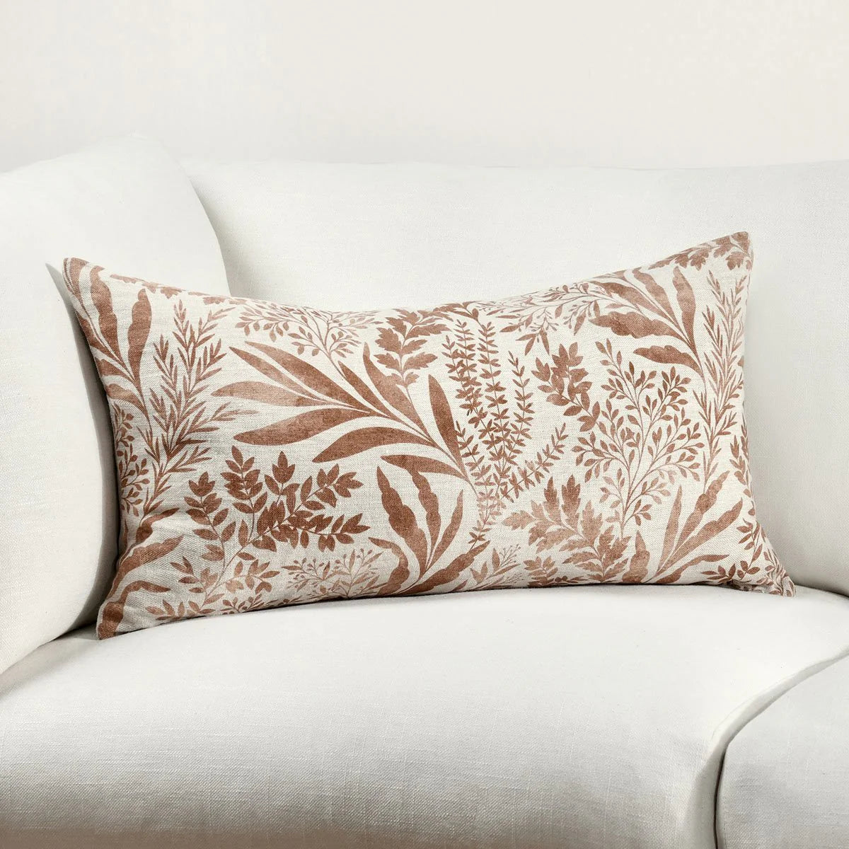 Decorative chestnut brown lumbar pillow with watercolor leaf pattern on a white sofa. 