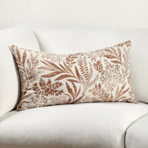 Decorative chestnut brown lumbar pillow with watercolor leaf pattern on a white sofa. 
