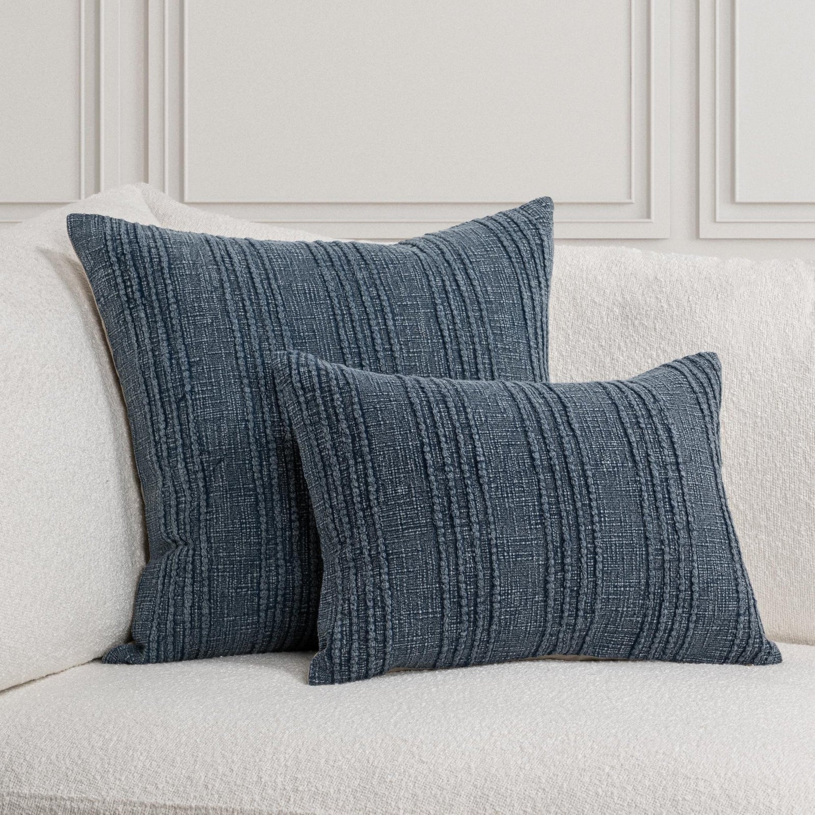 Twenty-two inch and lumbar decorative navy blue textured stripe pillows on a white sofa against a light gray wall.