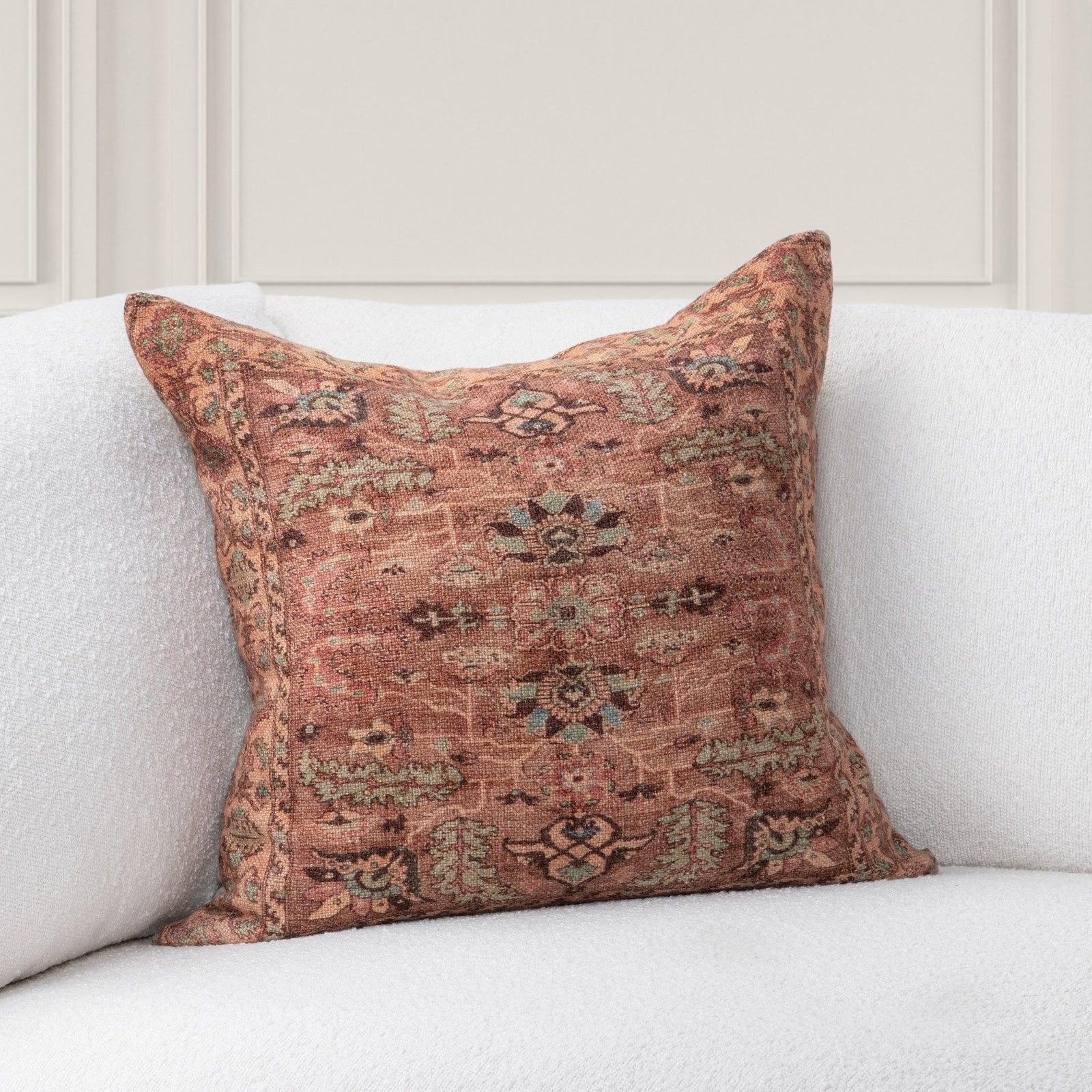 Decorative accent pillow with intricate greens, creams, browns, and burnt sienna colored patterns on a white sofa. 