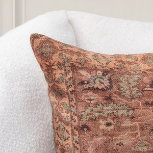 Close up view of decorative accent pillow with intricate greens, creams, browns, and burnt sienna colored patterns on a white sofa. 