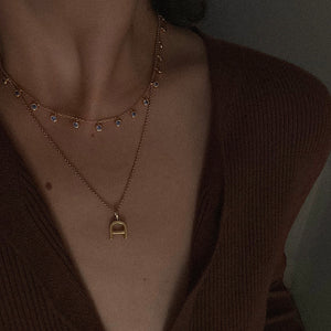 Cubic Zirconia Gold necklace layered with a letter 'D' pendant necklace on a person wearing a brown top.