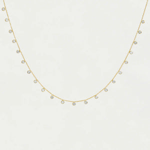 Gold necklace chain with small cubic zirconia pendants on a light gray background. 