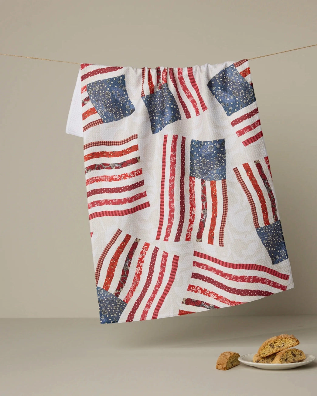 Red, white, and blue patchwork themed American flag patterned towel hanging on a line with cookies on a plate below.  Geometry House. 