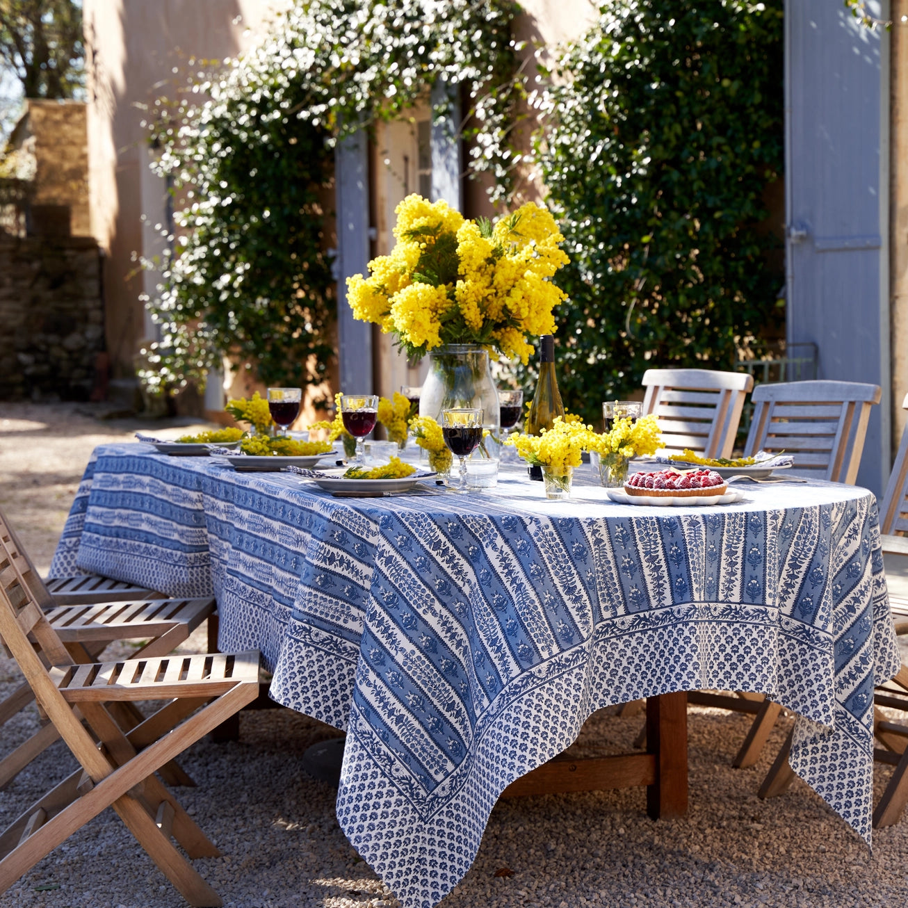 French inspired blue floral printed tablecloth with vibrant yellow blooms displayed across a outdoor dining table. 