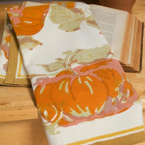Close up view of orange and mustard printed pumpkin tea towels displayed over an open book. 