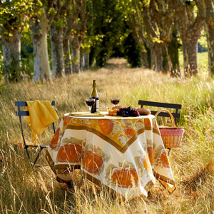 Round Autumn picnic set in a field surrounded by trees and various fruits displayed on table with wine. 