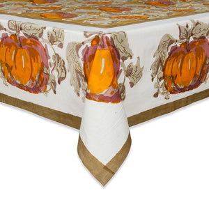 An ivory tablecloth featuring a warm autumn harvest pattern with large orange pumpkins, brown leaves, and a solid brown border, shown draped over the corners of a table against a white background.