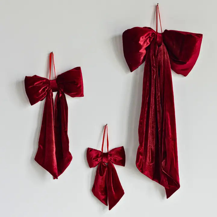 Three red velvet bows of different sizes hanging against a light gray background. 