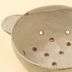 Close-up of a ceramic small berry colander with holes on a beige background
