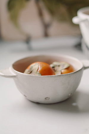 White ceramic fruit bowl with persimmons on a light surface