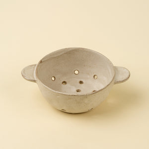 handmade stoneware fruit and vegetable colander bowl against beige background. 