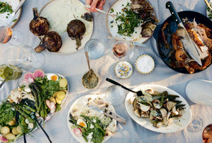 Diverse array of food on a table with various dishes and utensils photographed from cookbook "Rooted Kitchen" by Ashley Rodriguez. 