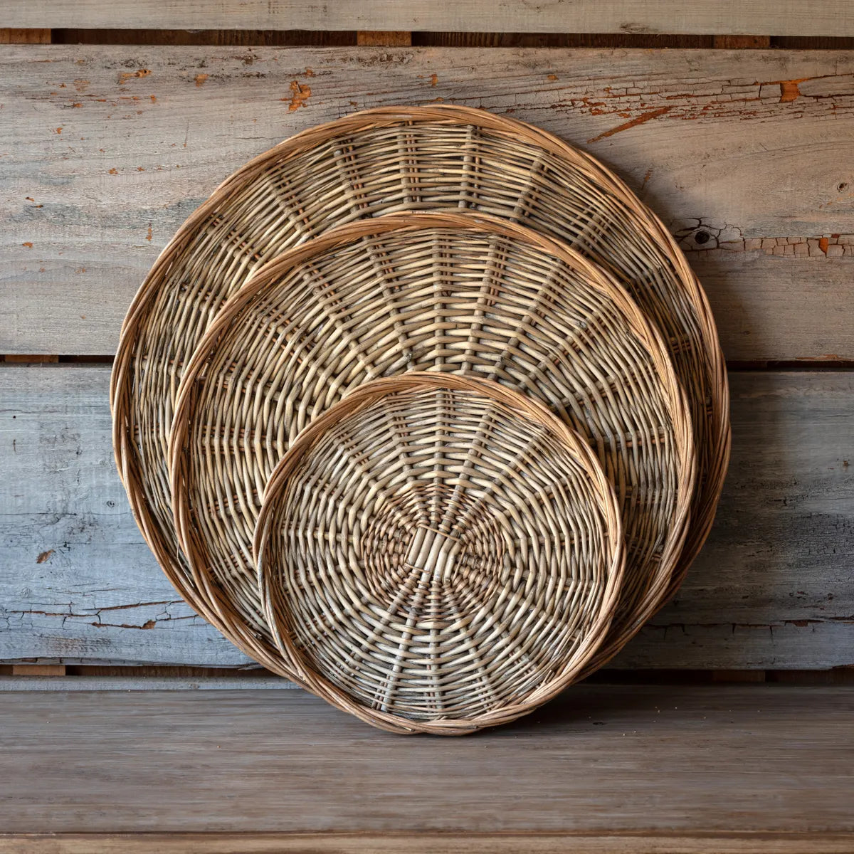 Small, medium, and large hand woven wicker basket trays displayed stacked against a shiplap wall. 