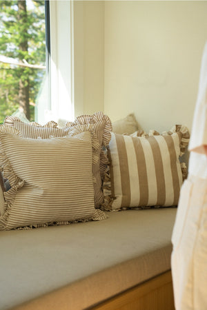 Striped ruffle edge linen/cotton pillows on a window seat bench with a view of trees outside.