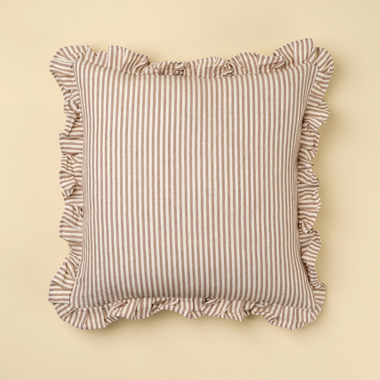 Striped linen and cotton pillow with ruffled edges on a beige background