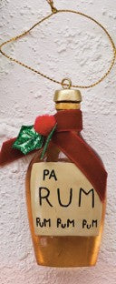 A decorative hanging ornament shaped like a bottle of rum, with a gold hanging loop, a brown ribbon, a small green bow, and a cream label reading 'PA RUM' and 'RUM RUM RUM'.