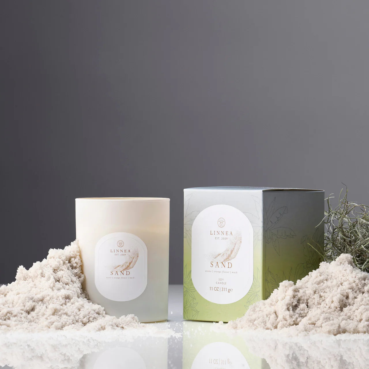 Sand scented candle on a textured surface with sand displayed against a dark background. Linnea soy wax candle. 