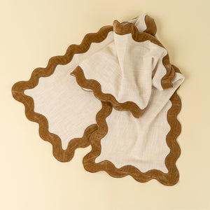 Cotton ivory table runner with gold  scalloped velvet edge on a beige background. 