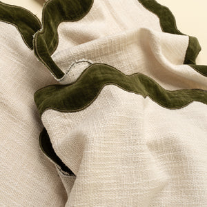 Close-up of a textured off-white woven fabric with wavy olive green velvet trim, draped to show the material and color contrast.