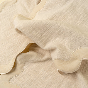 A close-up of a light beige woven textile with a scalloped edge and a slightly different, smoother beige lining or backing.