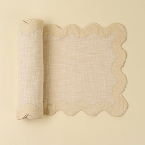 Rolled-up ivory table runner with scalloped velvet edge on a beige background. 