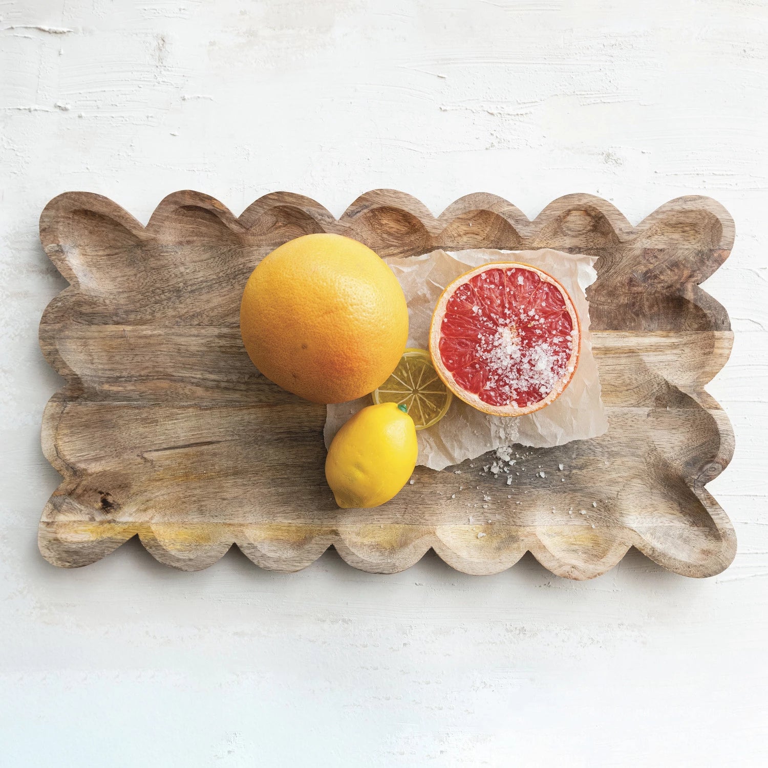 Scalloped mango wood tray with a half-sliced grapefruit, lemon, and orange on a white background