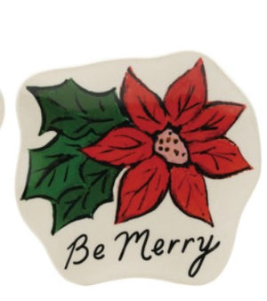 A ceramic Christmas ornament or plaque with a hand-painted poinsettia and holly design, featuring the text 'Be Merry' in black script on a cream-colored background.