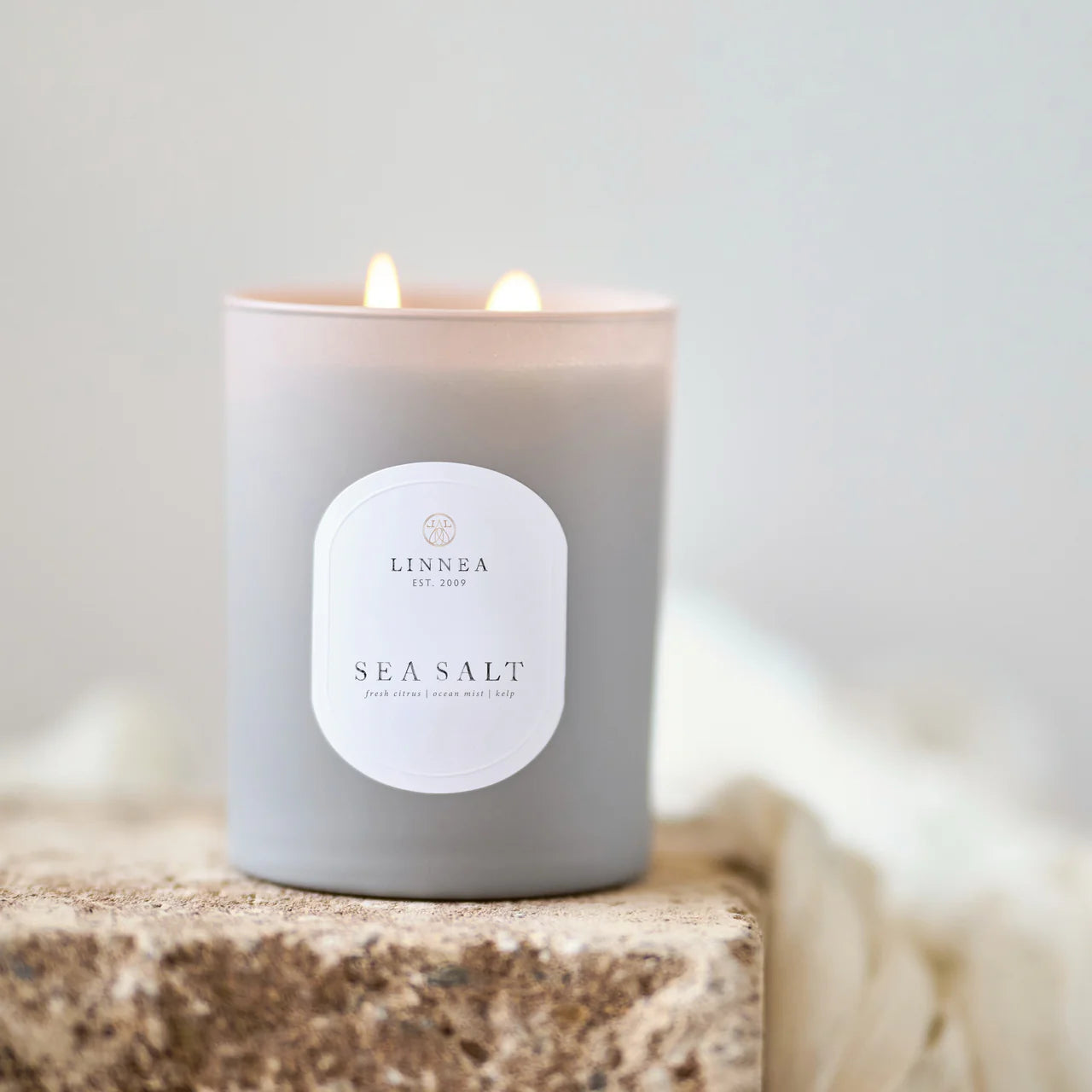 Lit candle with 'LINNEA' label on a textured surface