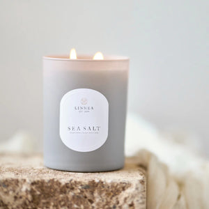 Lit candle with 'LINNEA' label on a textured surface