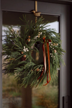 Seasonal holiday faux snowberry green wreath with trio of velvet ribbons hanging on a front door.
