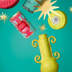 Colorful decorative items including a yellow vase, red bar soaps, and an individual green soap bar on a teal background.
