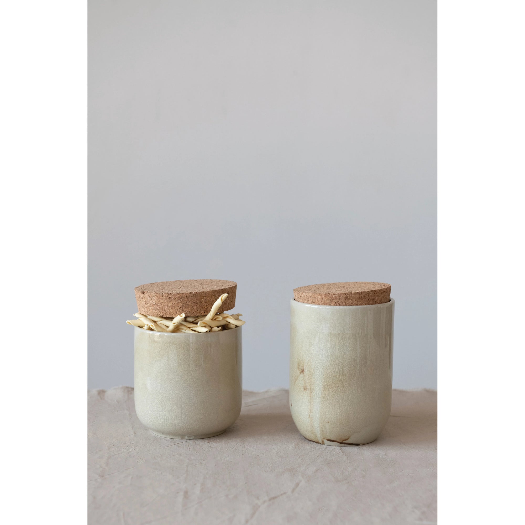 Set of two taupe swirled marble stoneware vases with cork lid. One is filled with dried pasta. 