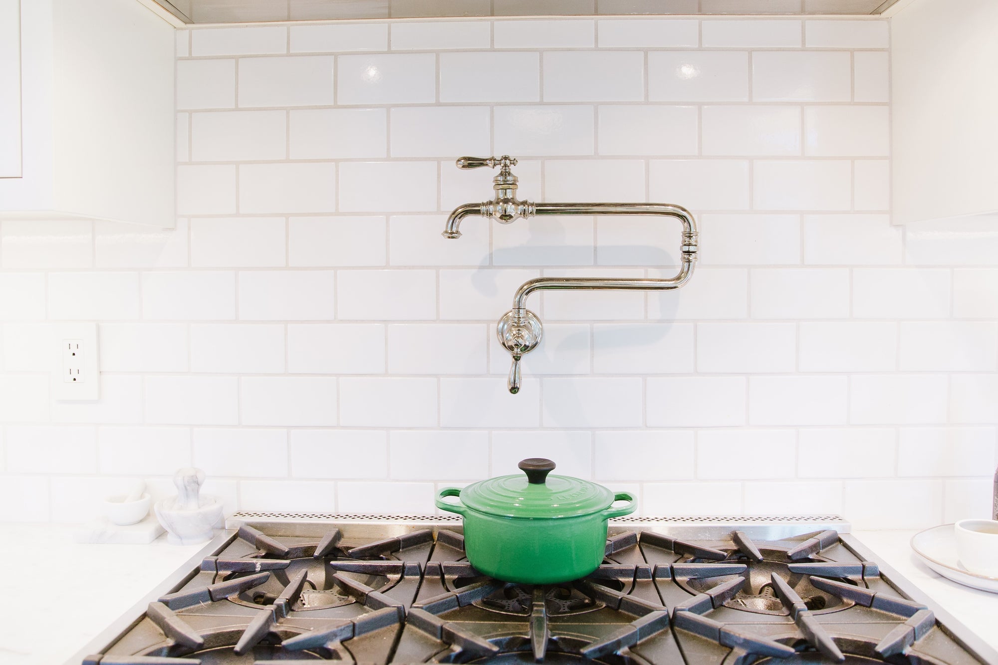 Pot filler over open range and green stock pot, with white subway tile