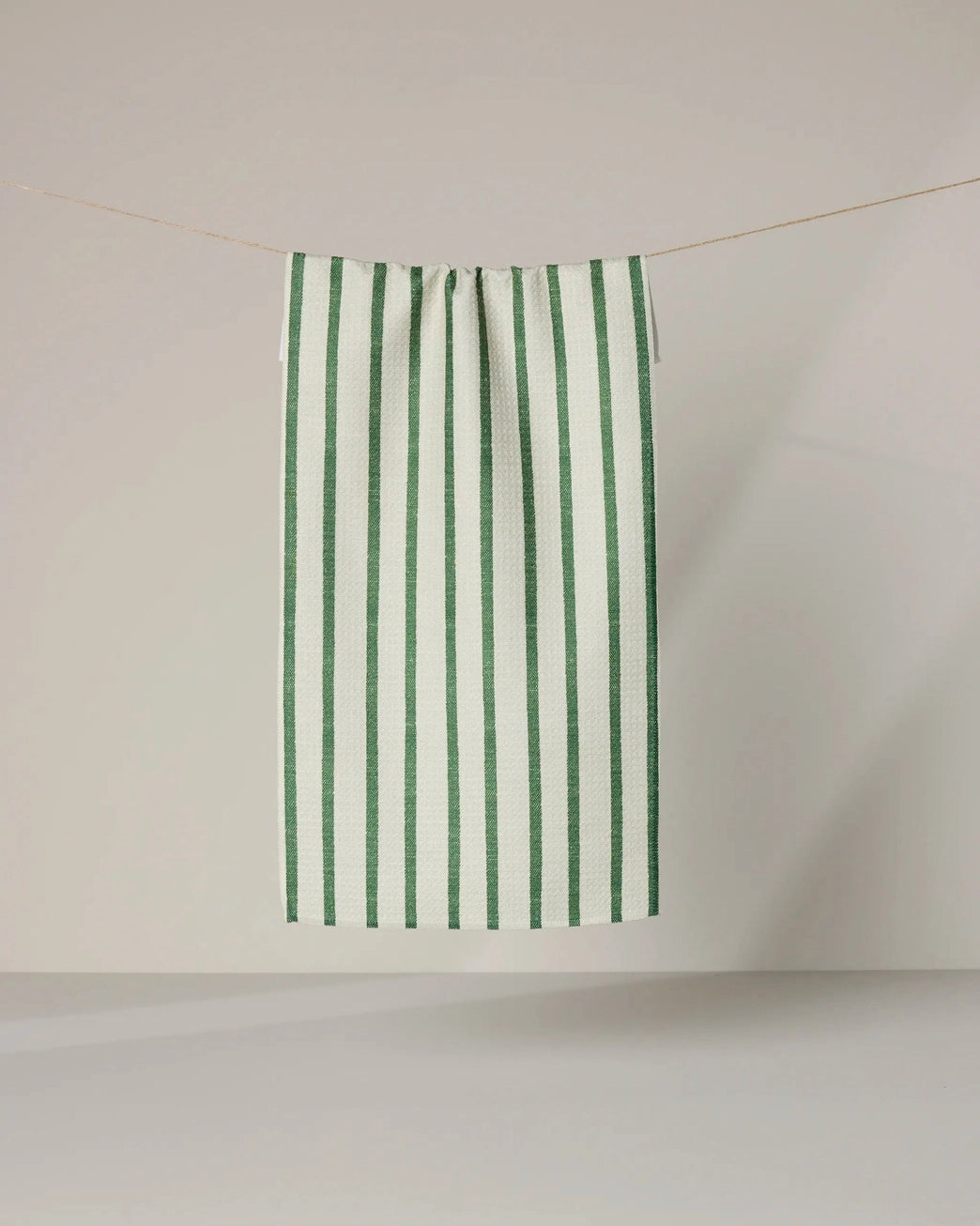 Kelly green and white striped bar towel hanging on a line against a plain background. Geometry House. 