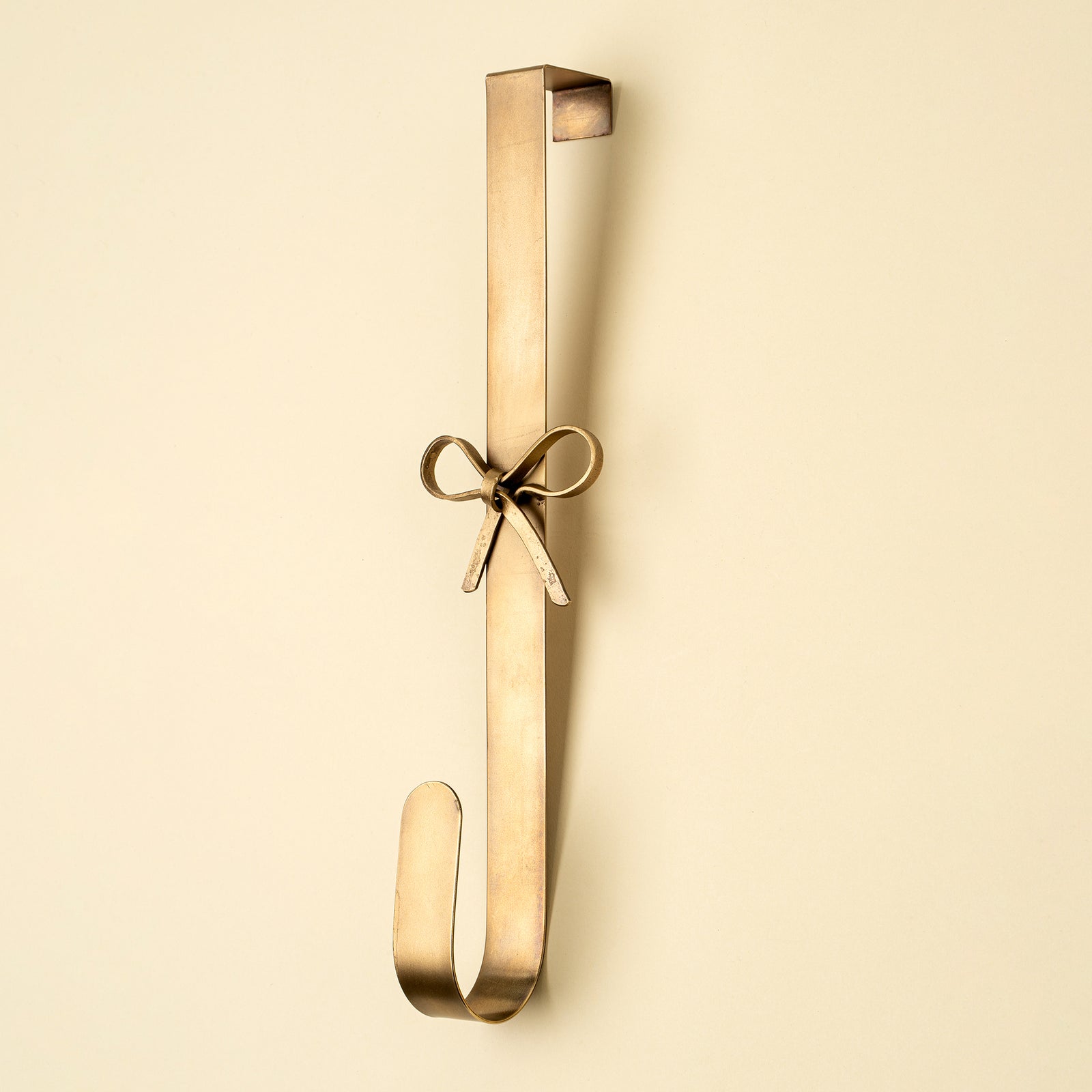 Gold decorative wreath holder with a tied bow in center against a beige background.